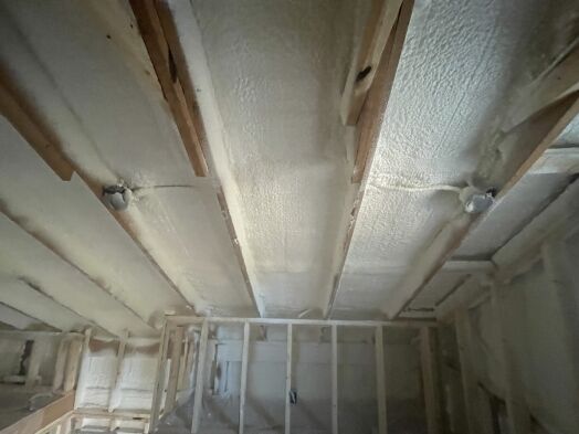 Ceiling with exposed wooden beams and spray foam insulation between the joists in a building under construction.