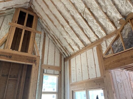 Interior of a house under construction with exposed wooden framing and spray foam insulation applied to the walls and sloped ceiling.
