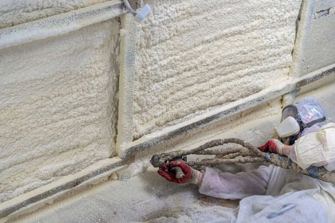 A worker in protective gear sprays polyurethane foam insulation onto a wall, creating an airtight and energy-efficient barrier.
