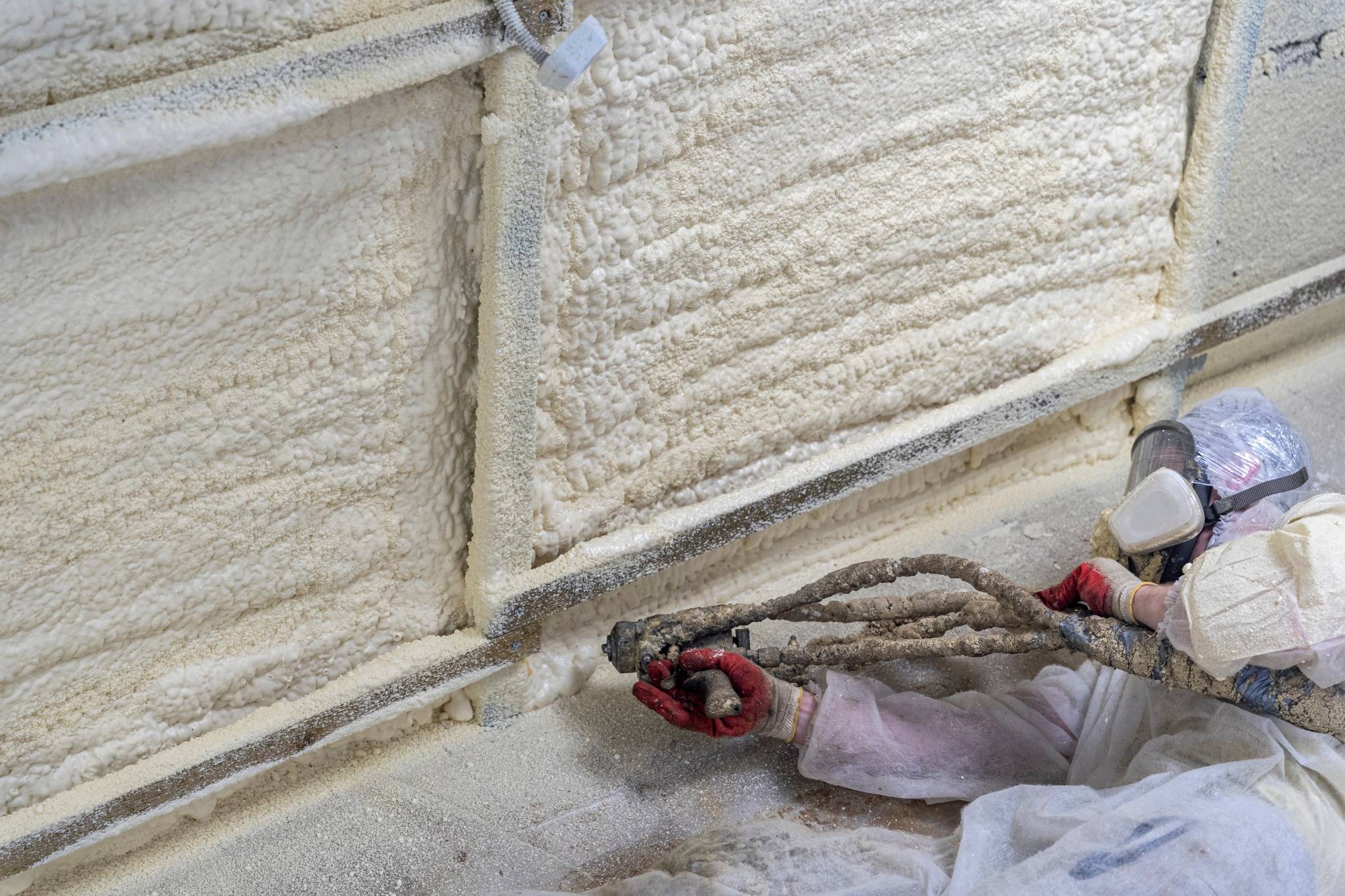 A worker in protective gear sprays polyurethane foam insulation onto a wall, creating an airtight and energy-efficient barrier.